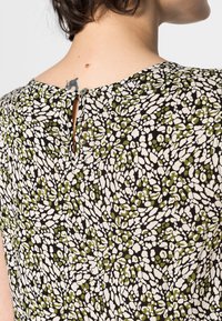 Haut à motif floral en tissu léger ; base noire avec des formes irrégulières vertes et crème. Présente une fermeture par ouverture en forme de serrure au dos.