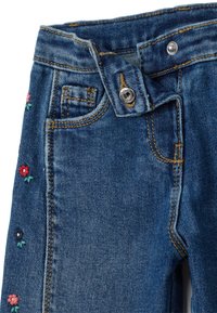 Vaqueros de mezclilla con un lavado azul oscuro, que presentan bordados florales en rojo, rosa y verde a lo largo del costado, y un cierre clásico de botón.