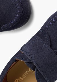 Chaussures en suede bleu marine avec une sangle Velcro et des coutures contrastantes. Bout arrondi et texture douce, dotées d'une semelle intérieure rembourrée.