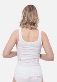 White cotton tank top with a scoop back, featuring a lace accent at the hem. Smooth texture and fitted design.