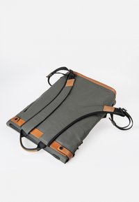 Grauener Rucksack mit braunen Lederakzenten, ausgestattet mit verstellbaren Trägern, strukturiertem Stoff und einer Reißverschlusstasche. Kompaktes rechteckiges Design.