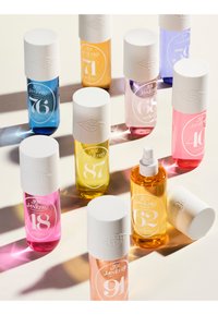 Tien flessen Sol Janeiro-geuren, in verschillende kleuren waaronder blauw, roze, geel en paars, met witte doppen en gegraveerde labels.