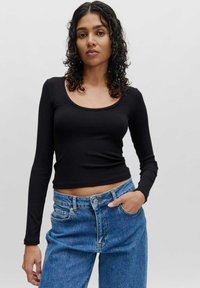 Schwarzes, geripptes Langarmoberteil mit einem scoopförmigen Ausschnitt, kombiniert mit hoch taillierten blauen Jeans. Das Outfit hat eine figurbetonte Silhouette.