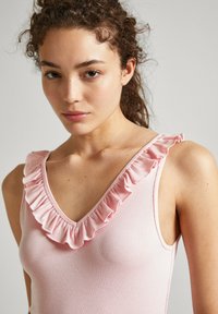 Top ribbed rosa chiaro con scollo a V e bordo arricciato lungo i margini, dotato di spalline sottili. Tessuto liscio, design aderente.