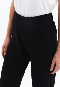 Pantaloni neri in maglia morbida con una larga fascia elastica in vita, caratterizzati da un finish testurizzato e una vestibilità slim, abbinati a una maglietta bianca.