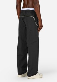 Črne, ohlapne hlače iz lahkega materiala z belim elastičnim pasom in kontrastnim belim robom na žepih.