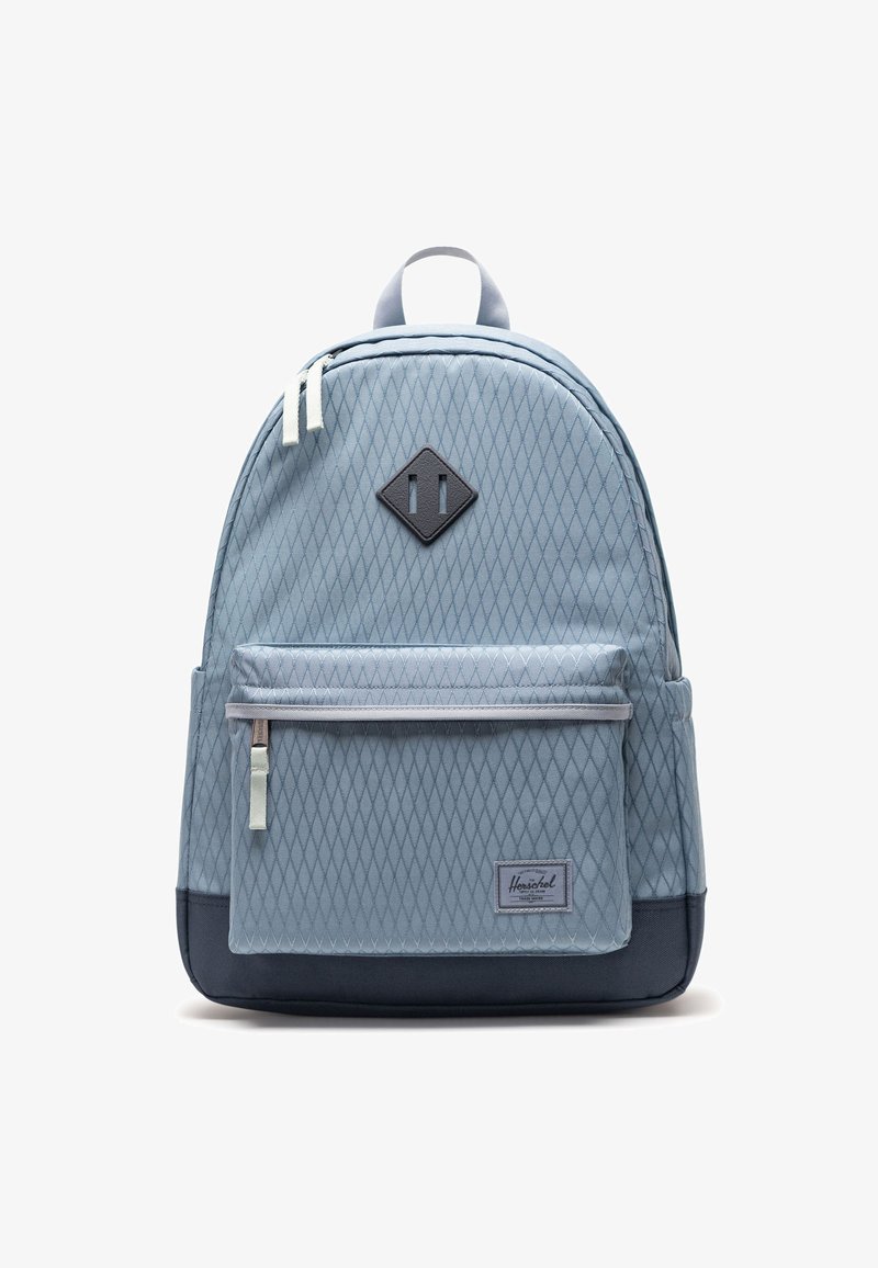 Sac à dos bleu clair avec motif en losange, poche avant zippée, fond noir et poignée supérieure, photographié sur fond blanc.