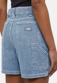Calções de ganga em azul claro com cintura alta, dois bolsos traseiros e um logótipo. O tecido apresenta um acabamento texturizado.