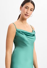 Robe sans manches à col bénitier en satin teal. Présente une texture lisse et des bretelles spaghetti réglables. Silhouette ajustée.