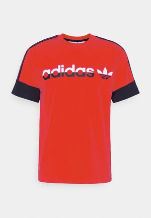 Rotes Adidas T-Shirt mit schwarzen Ärmelbündchen, schwarzen Streifen auf den Schultern und weiß-schwarzem Adidas-Logo sowie Kleeblatt vorne.