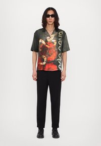 Μπλούζα με κοντό μανίκι και γιακά σε μαύρο χρώμα με κόκκινο λουλουδάτο σχέδιο και λευκό κείμενο. Συνδυάζεται με μαύρα φαρδιά παντελόνια και μαύρες μπότες.