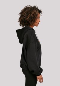 Black hooded sweatshirt with a relaxed fit, featuring a textured fabric, contrasting drawstring, and a small multicolored graphic on the chest.