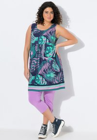 Sukienka bez rękawów w granatowym kolorze z zielonymi i różowymi tropikalnymi wzorami, zestawiona z lawendowymi legginsami 3/4 i ciemnoniebieskimi trampkami za kostkę.