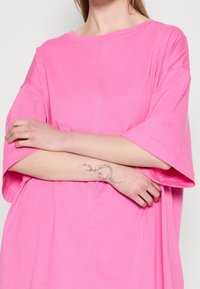 Camiseta grande rosa de manga corta, material de algodón, con un corte relajado, que presenta detalles de costura visibles y una textura suave.