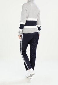 Grå och marinblå träningströja med vita ränder, hög krage och åtsittande ärmar, ihopparad med marinblå byxor med sidovita ränder och elastisk midja.