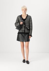 Svart og hvit tweed cardigan med frynser, gullknapper, kombinert med et svart skinnskjørt med knapper foran og svarte flate sko.