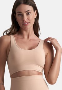 Reggiseno sportivo nudo realizzato in tessuto liscio, con ampia fascia, scollatura a giro e spalline sottili. Dettaglio a taglio accentuato sotto il busto.