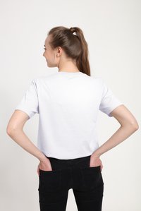 Bílé bavlněné tričko s krátkými rukávy a kulatým výstřihem, pohled zezadu. V kombinaci s černými džíny. Jednoduchý, neformální design.