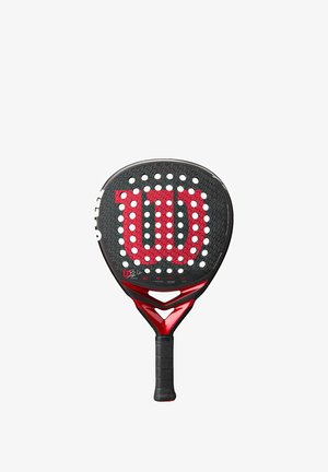 Wilson padel racket met een ronde kop, zwarte gestructureerde oppervlakte, rode accenten en grote witte perforaties, met een opvallend rood logo.