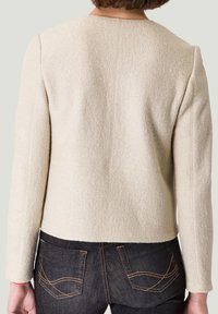 Beige wollen-blend jasje met een gestructureerde afwerking, voorzien van een eenvoudige ronde halslijn en een getailleerde snit. Draag het over donkere denim met contrasterende stiksels.
