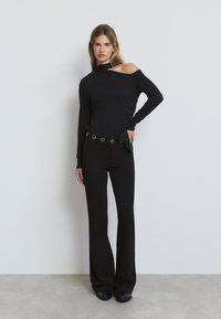 Haut noir à manches longues avec un design décolleté, associé à un pantalon noir évasé orné de rivets argentés sur la ceinture. Style minimaliste.