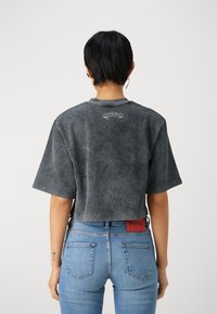 Camiseta negra, corta, de manga corta, con una textura desgastada y un logotipo blanco en la parte posterior. Combinada con jeans de mezclilla azules con una etiqueta roja.