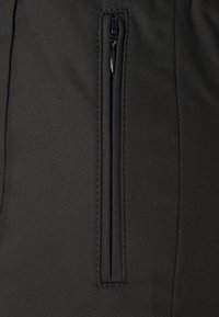 Tissu noir avec une poche zippée verticale noire cousue au centre, montrant un curseur de fermeture éclair partiellement fermé.