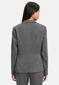 Szary żakiet w wzór houndstooth z wyciętymi klapami, dopasowany krój i wyraźnie zaznaczone ramiona. Teksturowana tkanina o subtelnym połysku. Przedstawiony widok z tyłu.