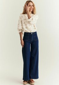 Lys blomstermønstrede bluse med flæser ved manchetterne parret med højtaljede, vide mørk denim jeans. Brune plateau sandaler fuldender looket.