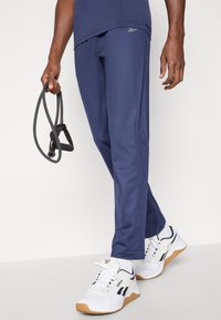 Ναυτικά αθλητικά παντελόνια από ελαφρύ ύφασμα με σχεδίαση που στενεύει προς τα κάτω και πλευρικές τσέπες, συνδυασμένα με λευκά αθλητικά παπούτσια με μαύρες λεπτομέρειες.