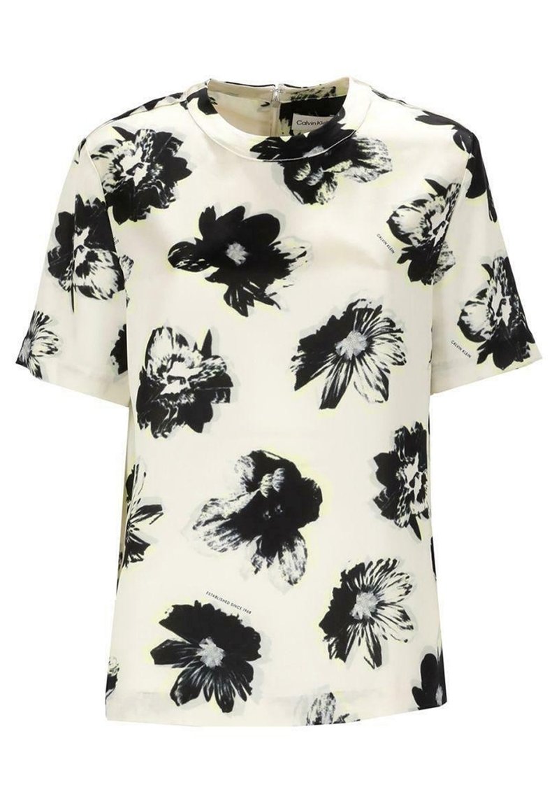 Blouse blanche à manches courtes avec un motif floral noir et gris, décolleté rond et fermeture éclair visible au dos.