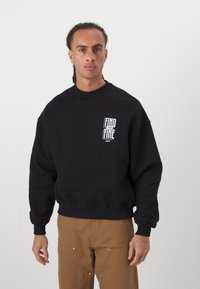 Svart sweatshirt med rund hals og senkede skuldre. Frontgrafikken har teksten "FIND" og "FINE." Stoffet virker mykt med en løs passform.
