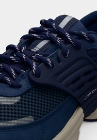 Σκούρο μπλε αθλητικό παπούτσι με υφασμάτινο δίχτυ και λαστιχένιες λεπτομέρειες. Διαθέτει κορδόνια με ρίγες και υφή στη φτέρνα με εμπορικό σήμα.