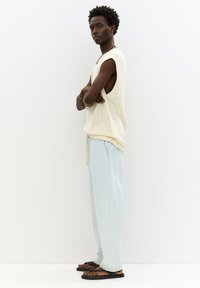 Ljust beige stickad ärmlös topp med stora armhål, matchad med ljusblå vida byxor och svarta flip-flops. En enkel, avslappnad look.