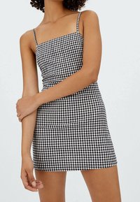 Sort og hvidt gingham mini-kjole med tynde stropper, tætsiddende liv og lige kant. Materiale i bomuldsblanding med en glat tekstur.