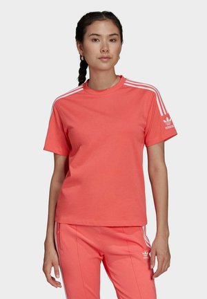 Camiseta de algodón color coral con cuello redondo, mangas cortas, detalles de tres rayas blancas en los hombros y pequeño logo de Adidas en la manga izquierda.