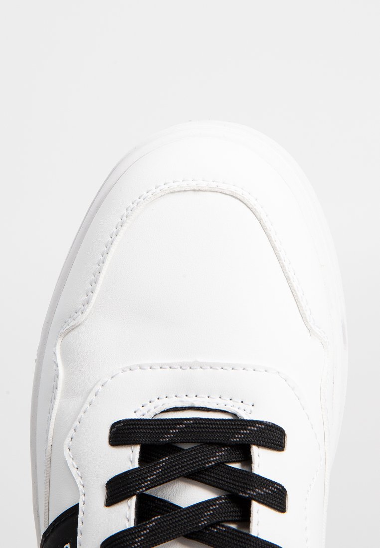 Zapatilla deportiva blanca con parte superior de cuero suave, cordones negros, puntera redondeada y costuras reforzadas en los laterales.