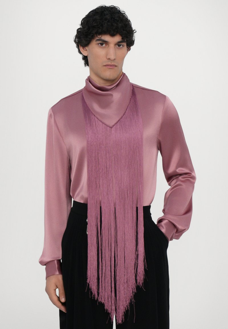 Haut en satin rose clair à manches longues avec un col haut et des franges à l'avant, associé à un pantalon noir. Texture lisse, design minimaliste.