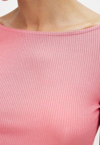 Rosa ribbad topp med vid halsringning, med en slät yta och subtil lyster. Nära vy framhäver tygets vertikala mönster.