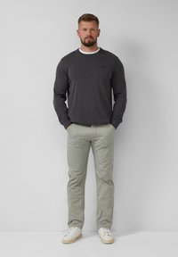 Grijze lange mouwen shirt met ronde hals, gecombineerd met lichtgroene broek. Witte lage sneakers met een beige zool. Eenvoudig, casual ontwerp.
