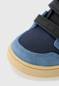 Modre semišne in mrežaste superge s črnimi Velcro trakovi in teksturirano gumijasto podplato. Okrogla kapica in kontrastni šivi.