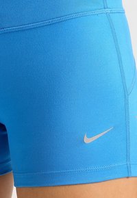 Niebieskie spodenki sportowe wykonane z elastycznego materiału, charakteryzujące się gładką fakturą i małym, srebrnym logo Nike na dolnej stronie.