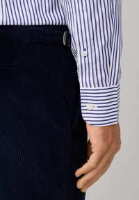 Himmelblau-weiße gestreifte Hemdärmel, kombiniert mit dunklen navy Cordhosen mit strukturierter Oberfläche und einer seitlichen Tasche.