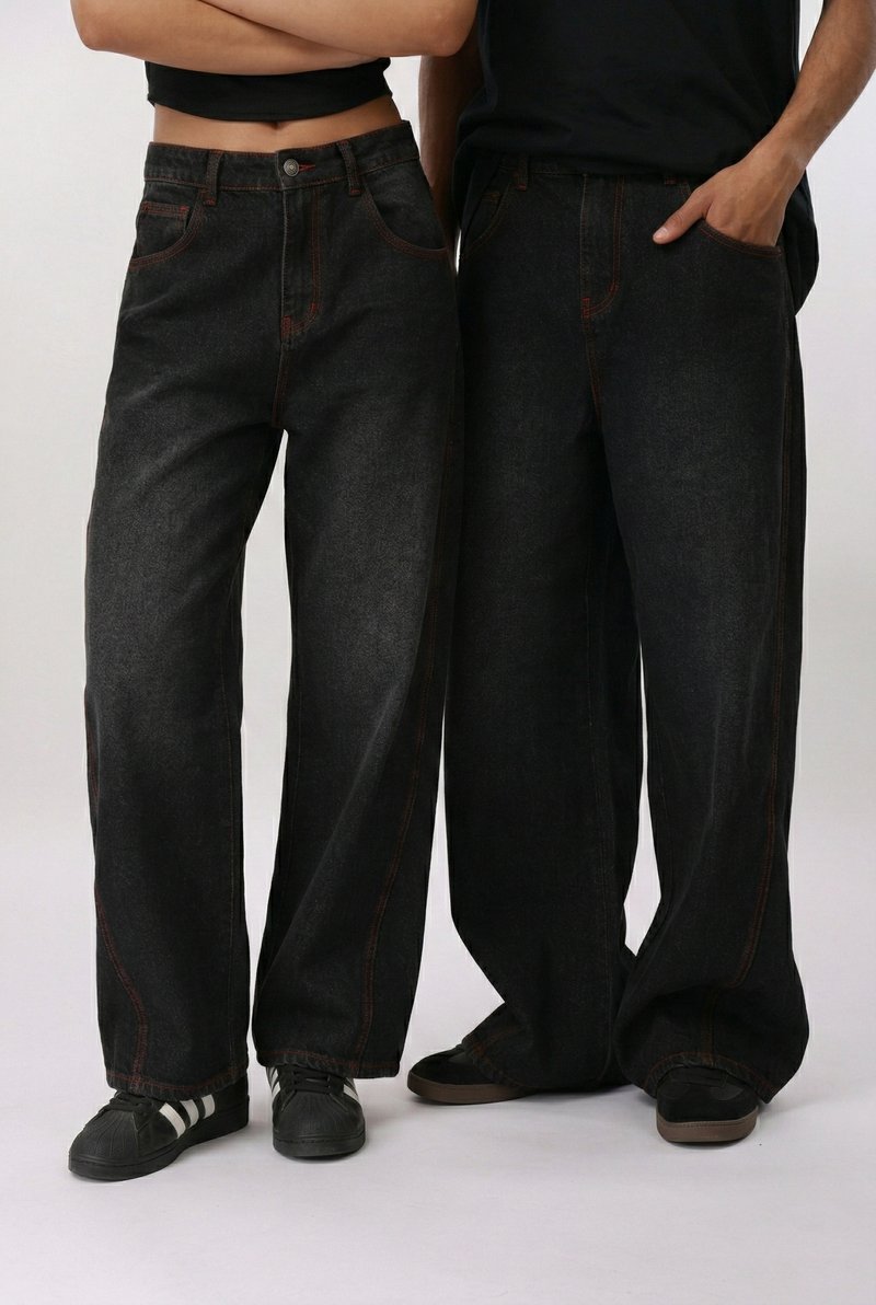 Δύο άτομα που φορούν φαρδιά μαύρα τζιν και μαύρα αθλητικά παπούτσια, ο ένας με σταυρωμένα τα χέρια και ο άλλος με το ένα χέρι στην τσέπη.