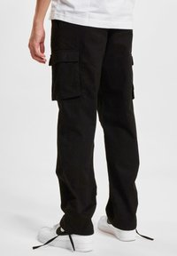 Black cargo pants made from sturdy fabric feature side pockets and a relaxed fit, paired with white sneakers. Matte texture, no visible patterns.