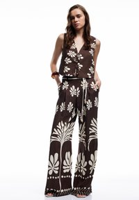 Braunes zweiteiliges Outfit mit einem kurz geschnittenen Oberteil im Blumenmuster und weit geschnittenen Hosen mit einem ähnlichen Design. Bänder betonen die Taille.