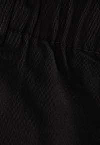 Mustaa corduroy-kangasta, jossa on pystysuorat urat. Saumassa on gathered-rakenne, mikä luo rypistyneen vaikutelman.