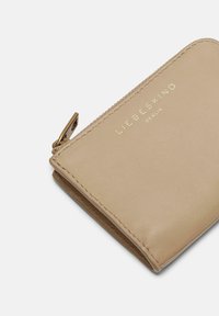 Beige Lederbörse mit Reißverschluss, ausgestattet mit einem goldenen Präge-Logo, glatter Textur und cleanem Design.