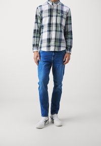 Camisa de cuadros en verde, blanco y azul marino; combinada con jeans azules y zapatillas blancas con detalles en negro. Corte recto.