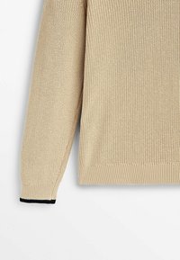 Beżowy dziergany sweter z długimi rękawami, ściągaczowymi mankietami i dołem. Posiada teksturowaną tkaninę oraz ciemnoniebieski akcent na mankiecie.